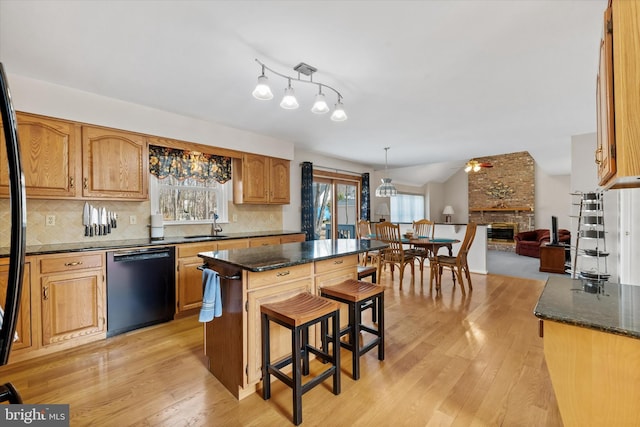 kitchen featuring light wood finished floors, backsplash, black dishwasher, a kitchen breakfast bar, and a fireplace