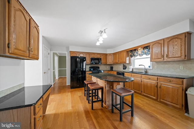 kitchen featuring black appliances, a breakfast bar, a sink, brown cabinetry, and light wood finished floors