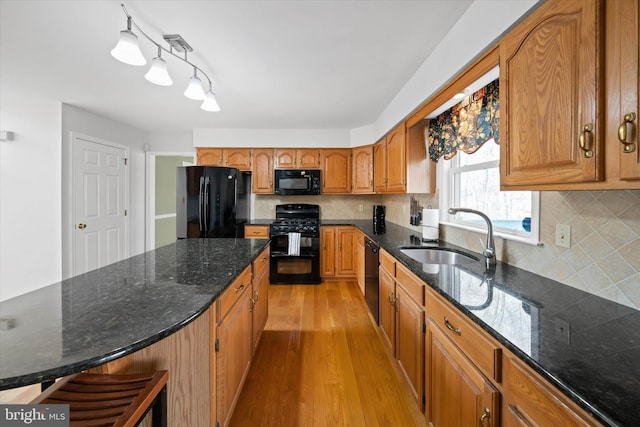 kitchen featuring brown cabinetry, light wood finished floors, a sink, black appliances, and backsplash