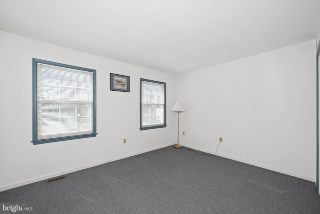 empty room featuring baseboards, visible vents, and dark carpet