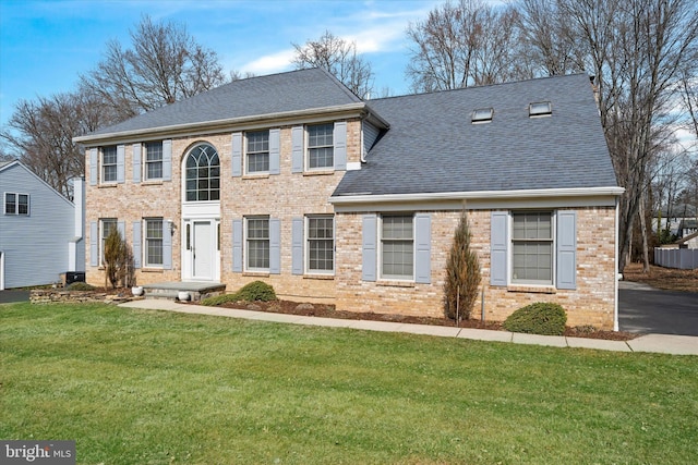 colonial inspired home featuring a front yard, brick siding, and roof with shingles