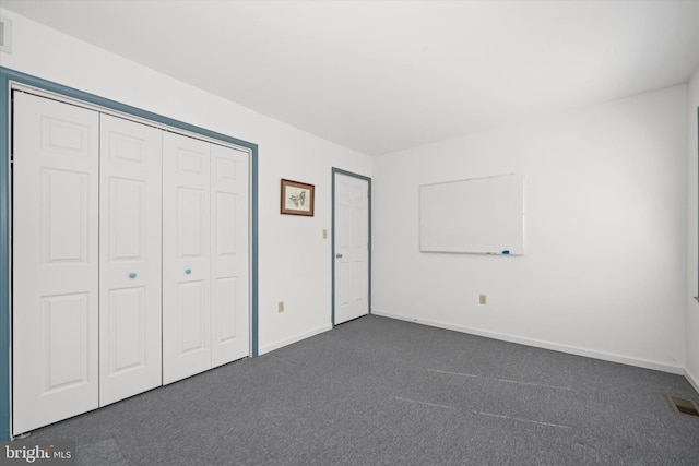 unfurnished bedroom featuring visible vents, baseboards, dark colored carpet, and a closet