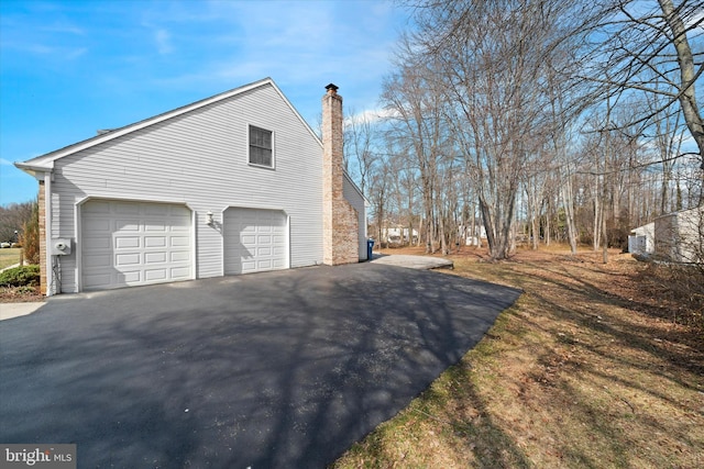 view of side of property featuring driveway, a chimney, and an attached garage