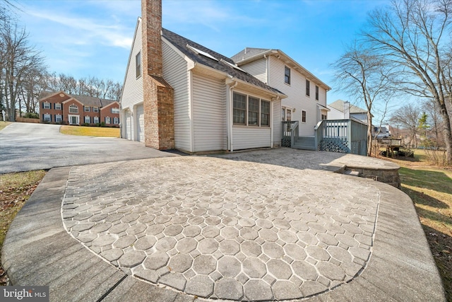 rear view of house featuring a wooden deck, driveway, an attached garage, and a chimney