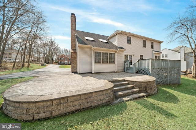 rear view of property featuring a wooden deck, a lawn, roof with shingles, and a chimney