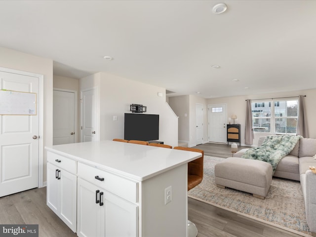 kitchen with wood finished floors, light countertops, white cabinets, open floor plan, and a center island