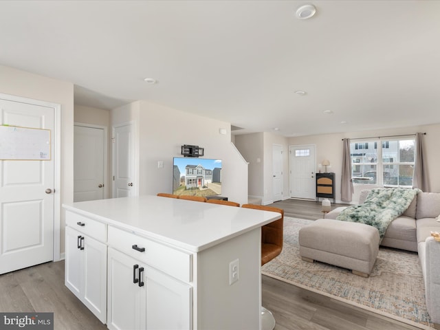 kitchen featuring wood finished floors, light countertops, white cabinetry, open floor plan, and a center island