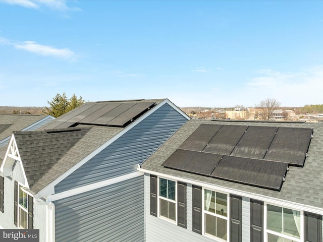 view of side of home with solar panels and roof with shingles