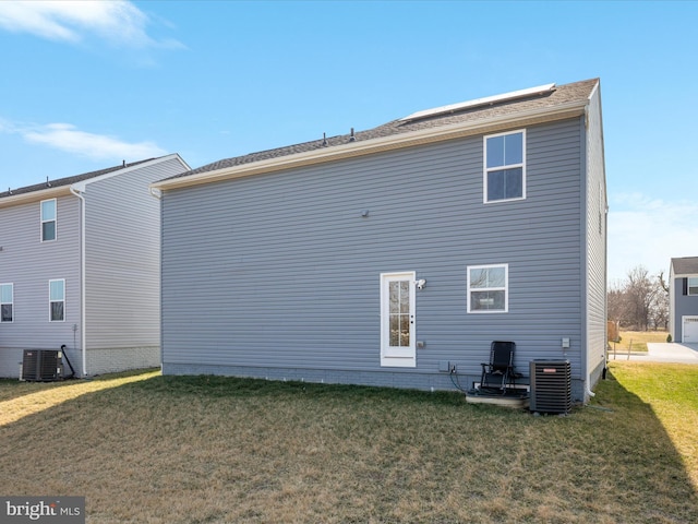 rear view of house with central air condition unit and a lawn