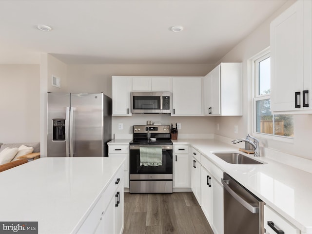 kitchen with a sink, stainless steel appliances, dark wood-type flooring, light countertops, and white cabinetry