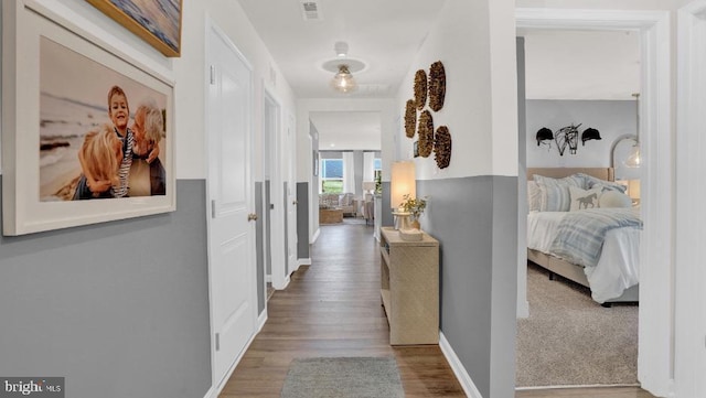 corridor with wood finished floors, visible vents, and baseboards