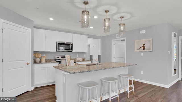 kitchen featuring dark wood finished floors, stainless steel microwave, white cabinets, and light stone counters