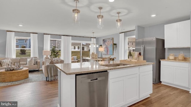 kitchen featuring light wood finished floors, a kitchen island with sink, a sink, white cabinets, and appliances with stainless steel finishes