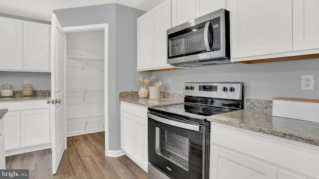 kitchen featuring light stone counters, white cabinets, appliances with stainless steel finishes, and light wood-style flooring