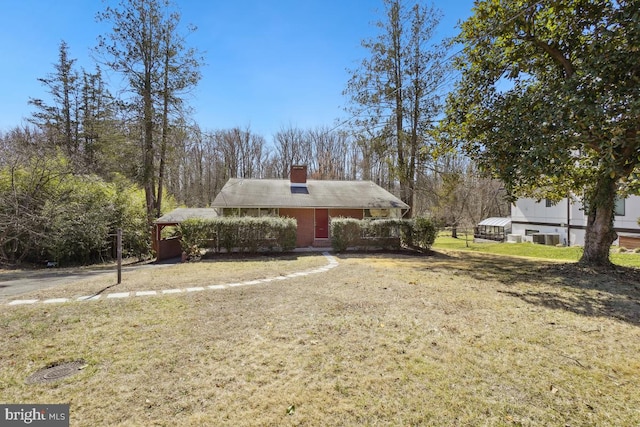 view of front of property featuring brick siding, a chimney, central AC, and a front yard