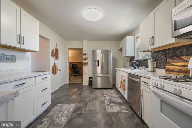 kitchen featuring tasteful backsplash, light stone countertops, white cabinets, stainless steel appliances, and a sink