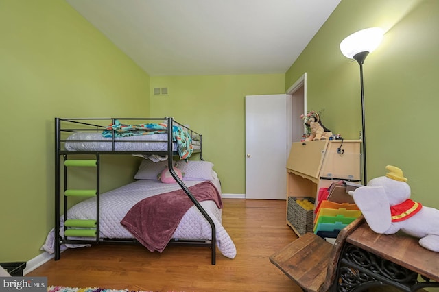 bedroom with visible vents, baseboards, wood finished floors, and vaulted ceiling