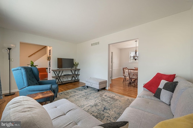 living area featuring a notable chandelier, wood finished floors, visible vents, and baseboards