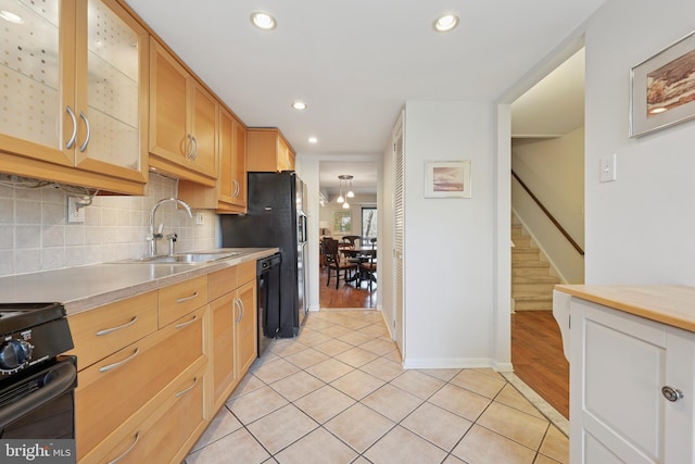 kitchen featuring tasteful backsplash, light countertops, light tile patterned flooring, black appliances, and a sink