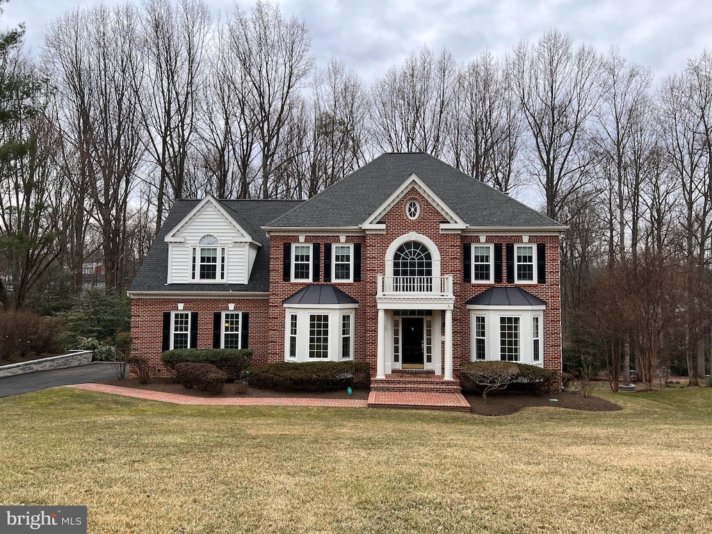 colonial inspired home featuring a front yard, brick siding, and roof with shingles