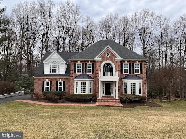 colonial inspired home featuring a front yard, brick siding, and roof with shingles