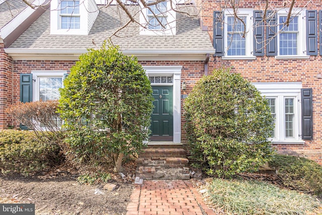 entrance to property with brick siding and a shingled roof