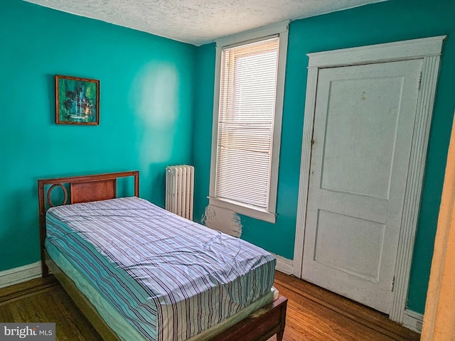 bedroom with radiator heating unit, wood finished floors, baseboards, and a textured ceiling