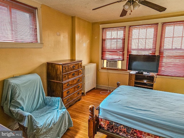 bedroom with cooling unit, radiator, a ceiling fan, and wood finished floors