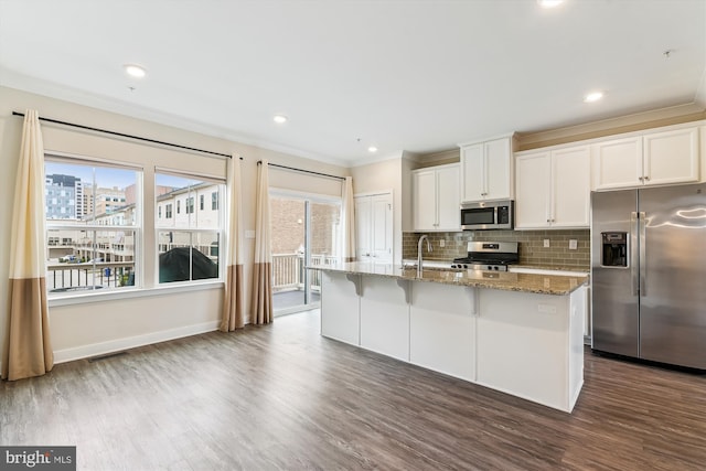 kitchen featuring light stone counters, an island with sink, dark wood-style flooring, appliances with stainless steel finishes, and backsplash