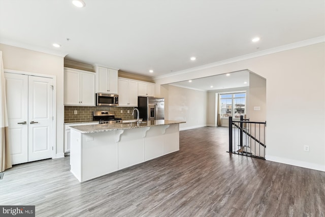 kitchen featuring an island with sink, light wood-type flooring, decorative backsplash, stainless steel appliances, and white cabinetry