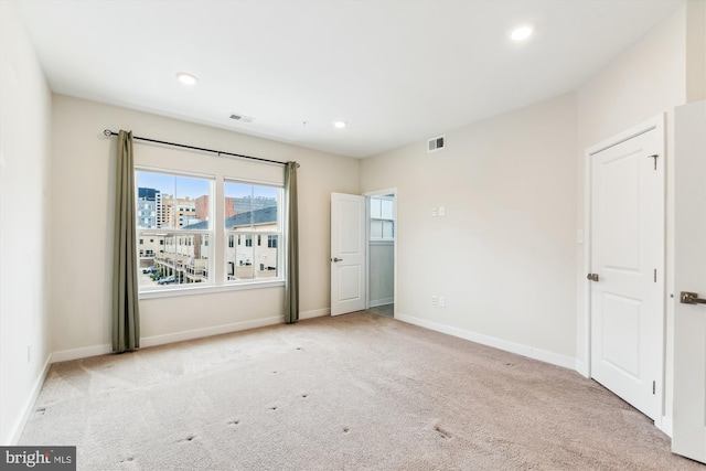 unfurnished bedroom with carpet, visible vents, baseboards, recessed lighting, and a city view