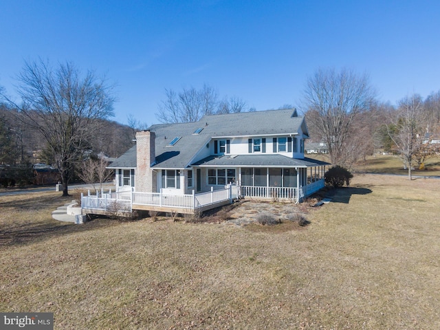 back of property featuring a wooden deck, a lawn, a chimney, and a sunroom