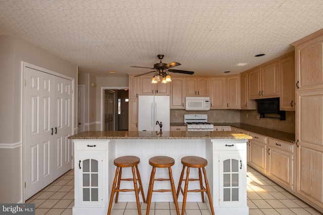 kitchen with a breakfast bar, light brown cabinetry, a kitchen island, tasteful backsplash, and white appliances