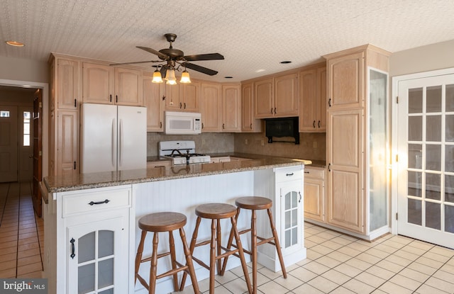 kitchen with a kitchen bar, white appliances, tasteful backsplash, and light brown cabinets