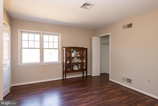 unfurnished bedroom with dark wood-style floors, visible vents, and baseboards