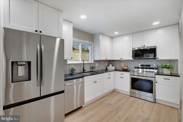 kitchen with a sink, backsplash, dark countertops, and appliances with stainless steel finishes