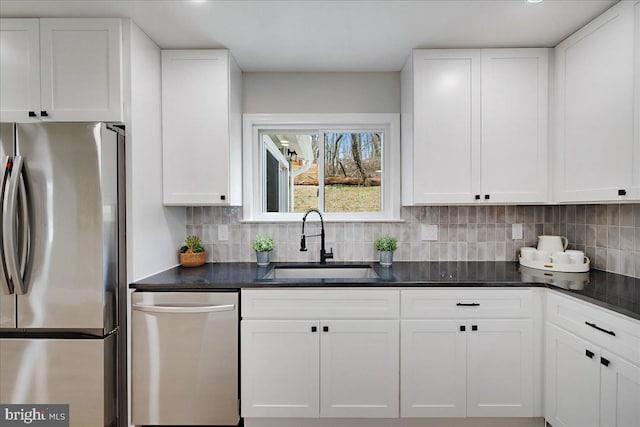 kitchen with a sink, dark countertops, stainless steel appliances, white cabinets, and decorative backsplash