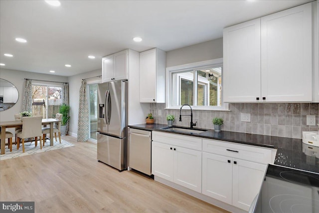 kitchen with light wood-type flooring, a sink, tasteful backsplash, white cabinetry, and stainless steel appliances