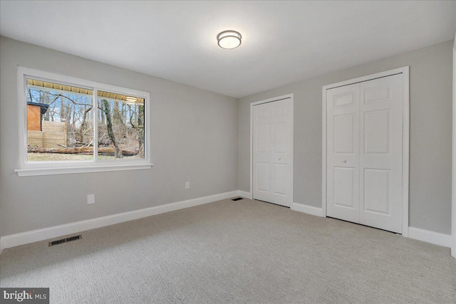 unfurnished bedroom featuring carpet flooring, visible vents, multiple closets, and baseboards