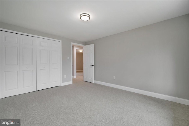 unfurnished bedroom with a closet, light colored carpet, and baseboards