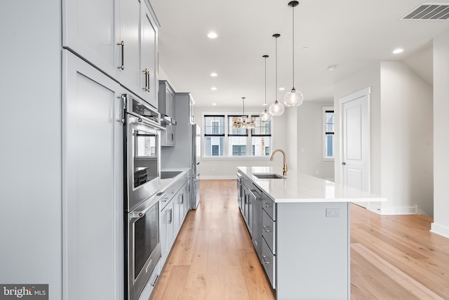 kitchen with a center island with sink, visible vents, light wood finished floors, gray cabinetry, and a sink