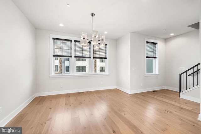 unfurnished dining area with a wealth of natural light, stairs, light wood-type flooring, and an inviting chandelier