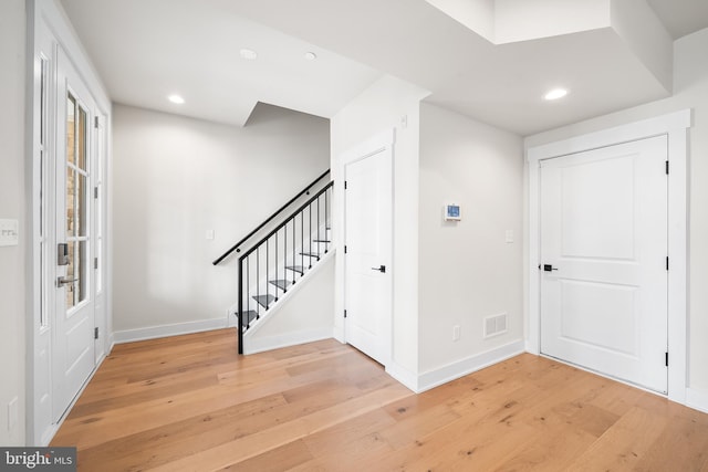 foyer with stairway, light wood-style flooring, baseboards, and visible vents