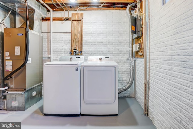 washroom with heating unit, laundry area, washing machine and dryer, and brick wall