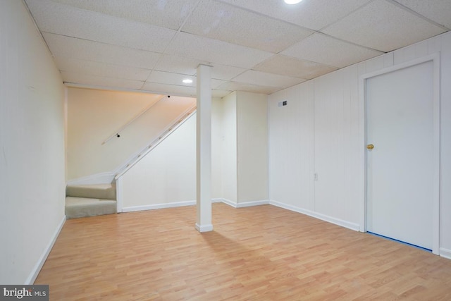 finished basement featuring baseboards, stairs, a paneled ceiling, and wood finished floors