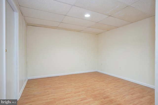 spare room with baseboards, light wood-type flooring, and a paneled ceiling