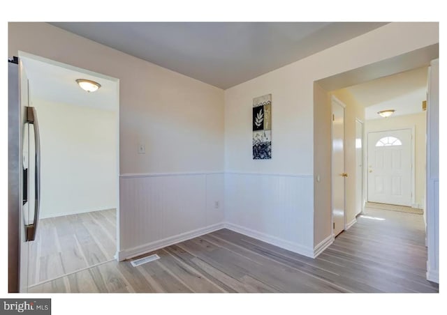 empty room with a wainscoted wall, visible vents, and wood finished floors