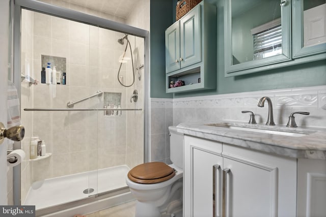 full bathroom featuring toilet, vanity, wainscoting, a stall shower, and tile walls