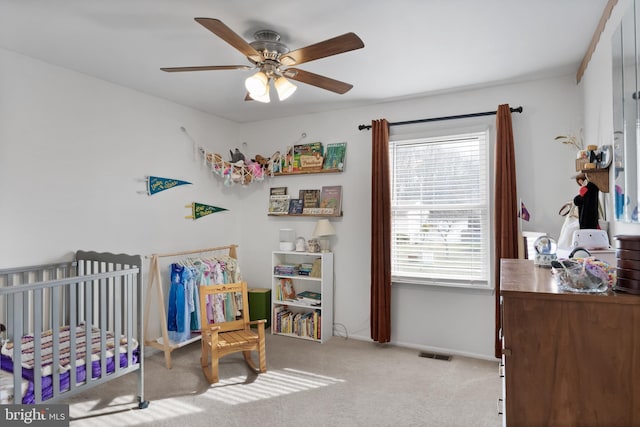 bedroom featuring visible vents, carpet floors, a nursery area, and a ceiling fan