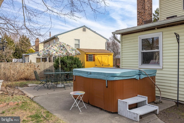 back of property with a storage unit, a hot tub, fence, an outdoor structure, and a patio area